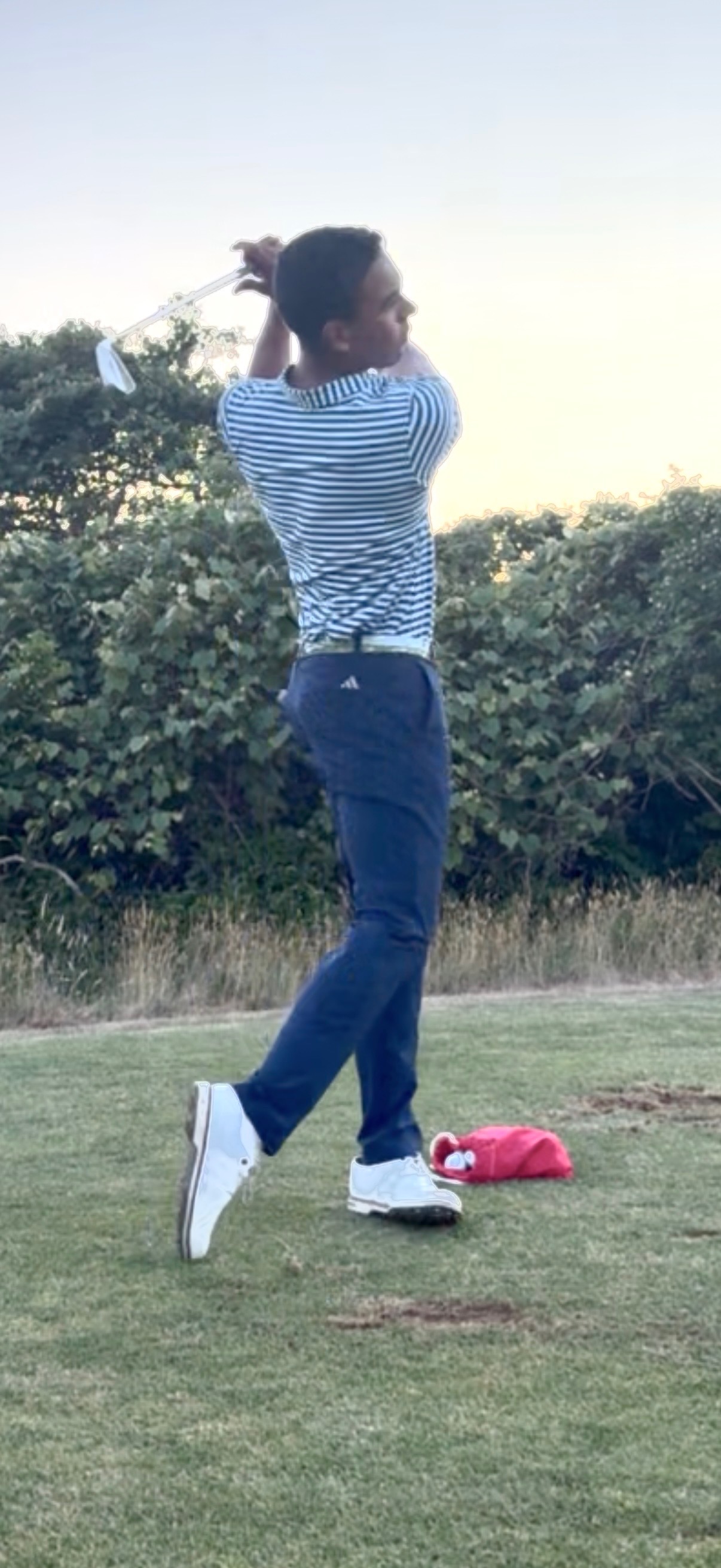 Junior golfer finishing a full swing at sunset